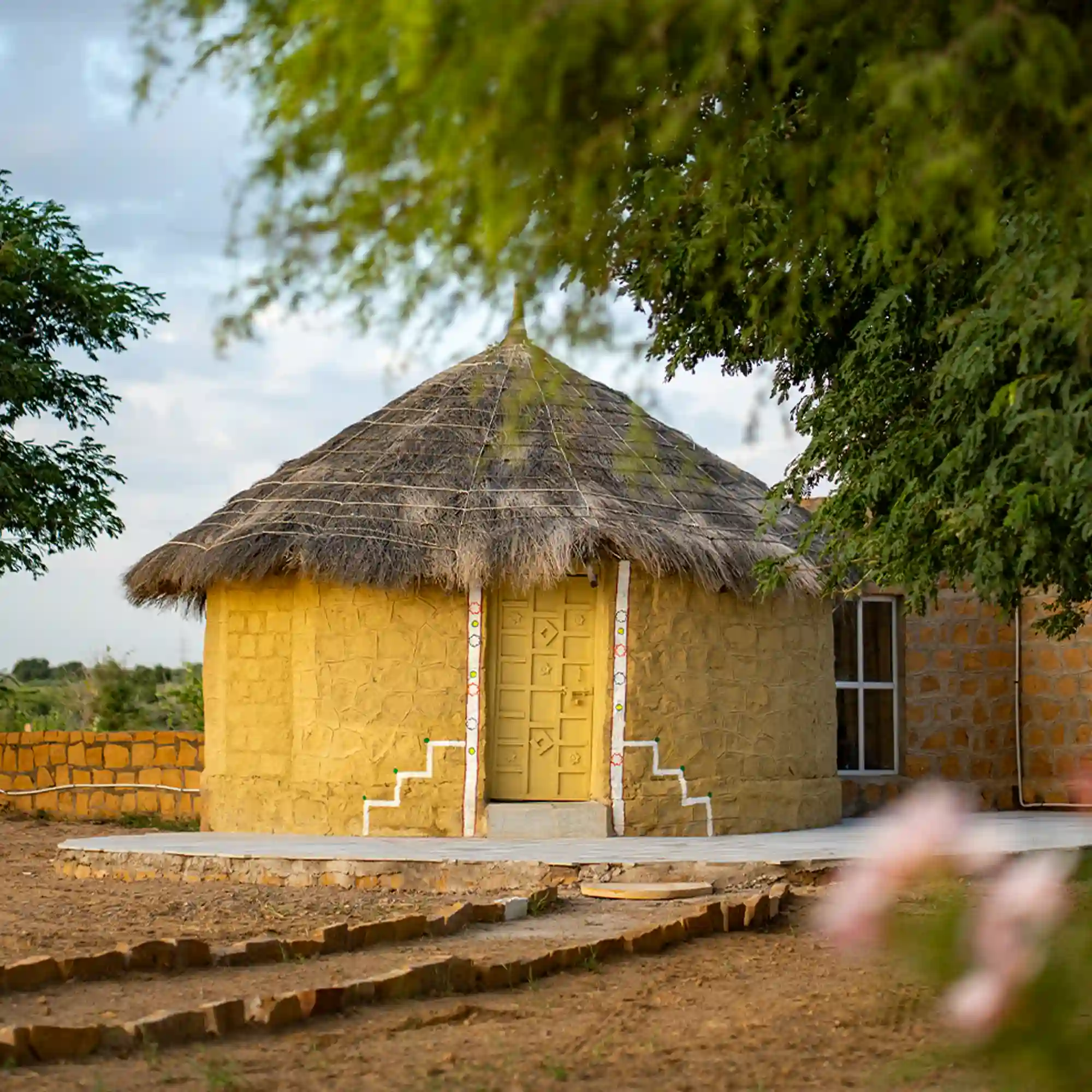 Traditional yellow stone mud cottage surrounded by greenery at Dreamtime Bungalows