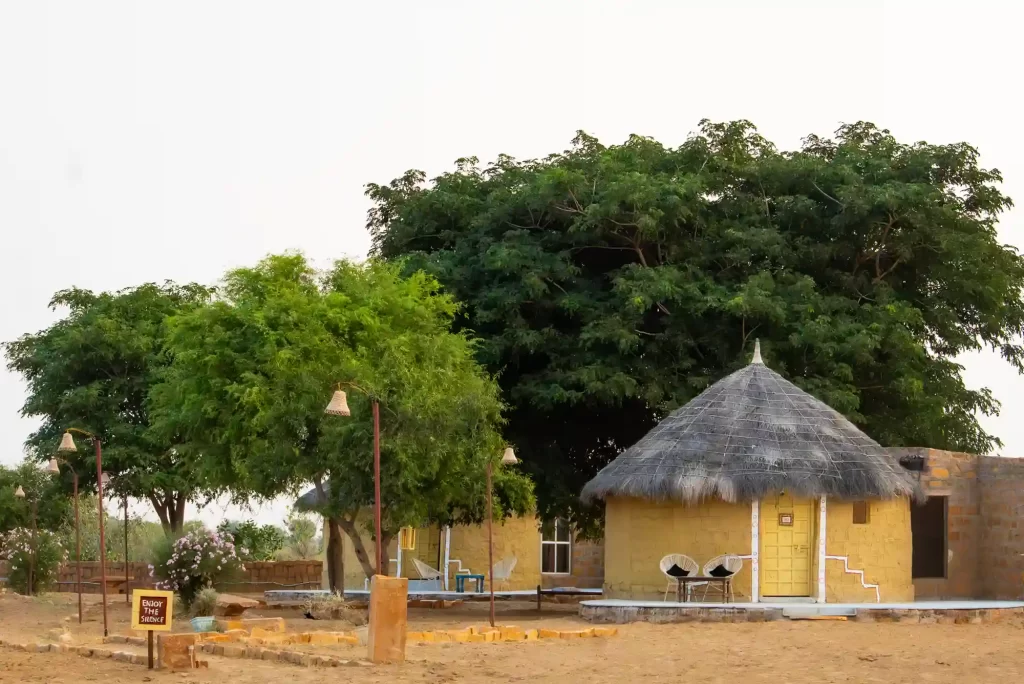 Rustic yellow mud cottages nestled under trees at Dreamtime Bungalows near Kuldhara